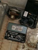 Photo showing corded circular saw in rusty brown color, Craftsman 14.4V drill in black plastic carrying case, and an 82-piece socket and ratchet set housed in a gray metal case with label.