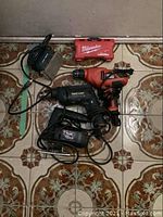 Four power tools including drills, sander, and jigsaw arranged on patterned floor tiles.
