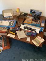 Overview photo of various boxed and loose model train items spread on a table, including an unboxed brass or black locomotive, track sections, and MRC Tech II controller in packaging.