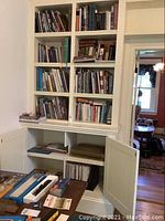 Built-in white bookshelf filled with various books and magazines placed on shelves and some stacked horizontally.