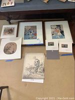 Overall view of the assortment of Asian art including framed and unframed prints and the two smaller wood block art pieces.
