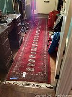 Full view of the long red wool tribal rug runner laid in a hallway, showing geometric medallion pattern and cream fringes at one end.