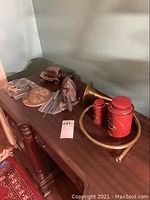 Wrought iron floor lamp with punched tin shade and various metal collectibles including collector coin banks, brass horn, and tins arranged on wooden furniture.