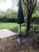 Full patio set showing folding table, two metal chairs, side table, umbrella and stand set in garden setting.