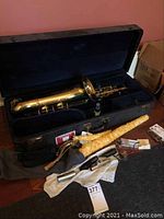 Open black hard case containing tenor sax body, neck, mouthpiece, strap, cleaning cloth and cork grease