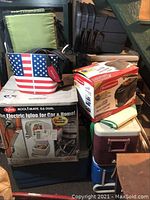 Photo showing stacked coolers, cooler bags including one with American flag print, and two green folding lawn chairs.
