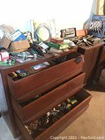 Wooden tool cabinet with several open drawers containing assorted hand tools and hardware items on top and inside the drawers.