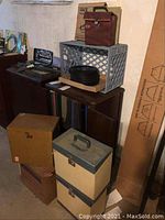 Overview of various record cases stacked including a plastic milk crate with records, cardboard boxes, and vinyl cases.