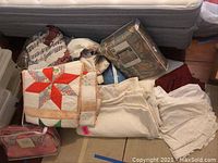 Photo showing folded quilts and bedding packaged and loose on floor near mattress.