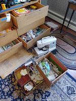Sewing machine on floor beside open drawers and boxes of craft supplies (thread, buttons, fabric).