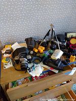 Tabletop view showing Nikon, Konica and Olympus SLR bodies with assorted film boxes, tripod and accessories
