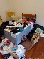 Full view of single wooden headboard bed with mattress, box spring, and assorted clothing and household items on it and around base.
