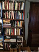 Bookshelf showing multiple shelves filled with thick and thin art-related books, some stacked horizontally, others upright.