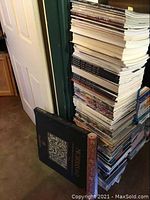 Tall stack of magazines leaning against a door and wall, including large issues and art related periodicals