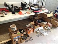 Wide shot of multiple boxes and assorted tools on a table and on the floor.