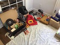 Overview of welding and grinding items including helmet, gloves, face savers, and boxes of grinding discs and accessories laid on floor near window.