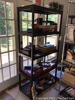 Full view of one black plastic shelving unit with 5 shelves loaded with assorted items.
