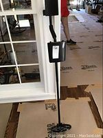 Photo showing the full height metal detector standing upright, displaying its circular search coil and arm rest.