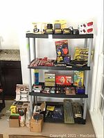 Full view of shelving unit with DeWalt battery packs, chargers, Drill Master chargers, reseating tools, drill bits, jaw puller set, riveter, air duster, adapter kit.