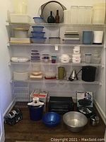 Shelf with many plastic storage containers, bowls, kitchen appliances, and accessories including Black and Decker toaster oven and Rival ice cream maker