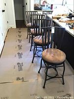 Four metal frame bar stools with tan suede-like round swivel seats lined up along a kitchen counter.