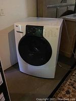 Full front view of the washing machine showing the black circular door and control panel above it.