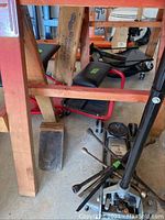 Floor jack, tire irons, creeper and seats arranged under wooden workbench.