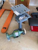 Full view of green grinder/buffer mounted on gray metal stand with platform and tray.