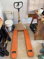 Full view of orange pallet jack leaning against wall in garage