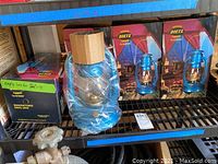 Shelf with four Dietz lanterns, two boxed, two partially wrapped in plastic, blue color with metal construction.