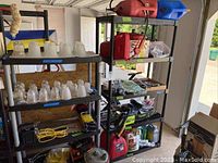 Wide shelf view showing red gas cans, blue kerosene can, assorted plumbing and workshop items on black Rubbermaid shelving.