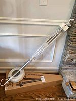 Full view of the white swing arm magnifying lamp with clamp base positioned against a wall showing the adjustable arm and lens.