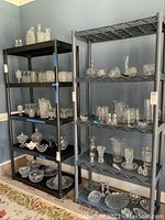 Two shelving units side by side; black vented shelves and gray solid shelves, both holding decorative glassware (not included).