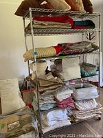 Full view of assembled metal shelving unit with multiple shelves filled with folded linens and pillows.