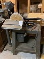 Front view of the bench grinder unit showing the grinding wheel, metal bench frame, and attached light.