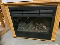 Front view of the electric heater inside an oak wood cabinet showing the front grille and simulated log fire bed.
