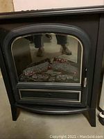 Front view of one electric stove heater showing black metal body and glass front panel with glowing ceramic logs inside.