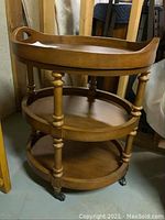 Front and side view of the three-tier solid wood serving cart with round lift-off tray on top and two round shelves below, sitting on metal casters.