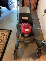 Front-top view of the mower showing red engine cover, steel deck, and attached rear bagger