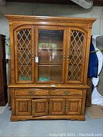 Full front view of oak china cabinet showing three glass doors with lattice work on side doors and central glass door, upper cabinet section and lower cabinet with drawers and doors.