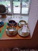 Wide shot of all four teacup and saucer sets on wooden ledge
