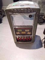 Full front view of dispenser showing embossed logo, coin slot and glass panel