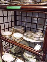 Shelf with stacked dinner plates, smaller plates, cups and saucers and a platter underneath.