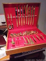 Full view of the gold plated flatware set in a wooden box with a red fabric interior, showing knives, forks, spoons, and serving utensils.