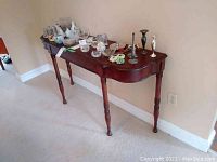 Wooden console table against a wall with various decorative items on top (not included).