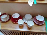 Wide view showing multiple vintage teacups and saucers including floral and gold designs, pink Aynsley saucer, and small white cups
