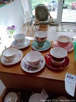 Image of seven porcelain teacups and saucers on wooden surface inside a room with some furniture in background
