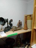 Photo of shelf with antique cast iron bell with rooster design, cast iron dentist themed coin bank, wooden pestle, and ceramic crock.
