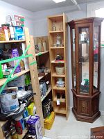 The shelving unit standing against a wall surrounded by various household items and a glass cabinet.