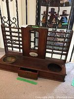 Front view of the antique British train ticket selling device showing wood base with two recessed bowl areas, a drawer, and ticket sorting racks on each side with brass fittings and missing bowl.